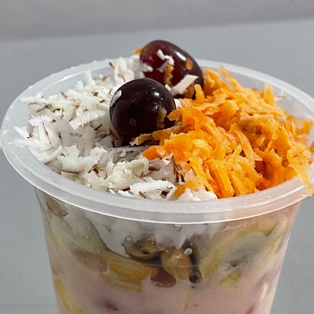 A cup of fruit salad topped with grated carrot and coconut