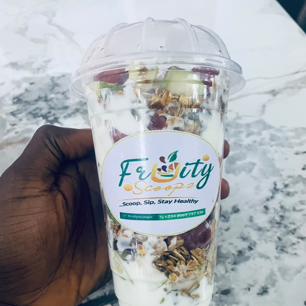 A fruit parfait cup with a Fruity Scoopz label, held in one hand